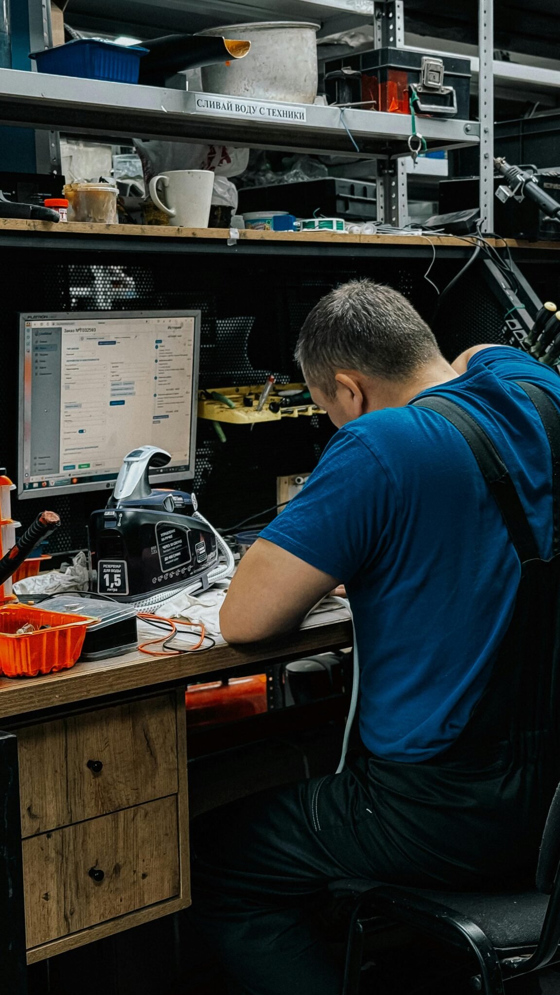 Technician focused on computer repair in cluttered workshop setting.